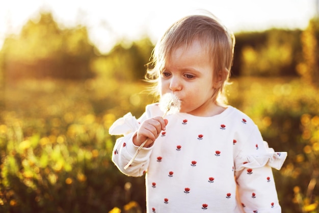 Bambina che soffia su un dente di leone in un campo