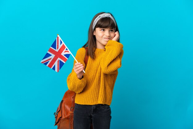 Bambina che studia inglese isolato su sfondo blu frustrato e che copre le orecchie