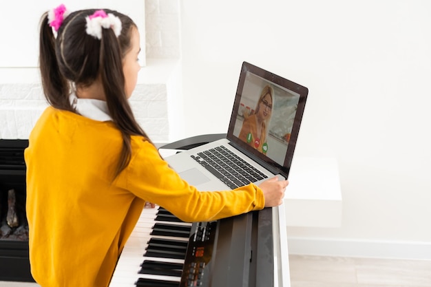 Bambina che suona il pianoforte. Lezione di musica online con insegnante tramite laptop.