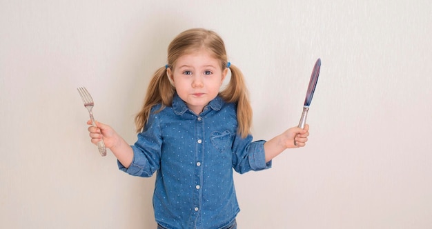 Bambina che tiene forchetta e coltello Bambino affamato divertente