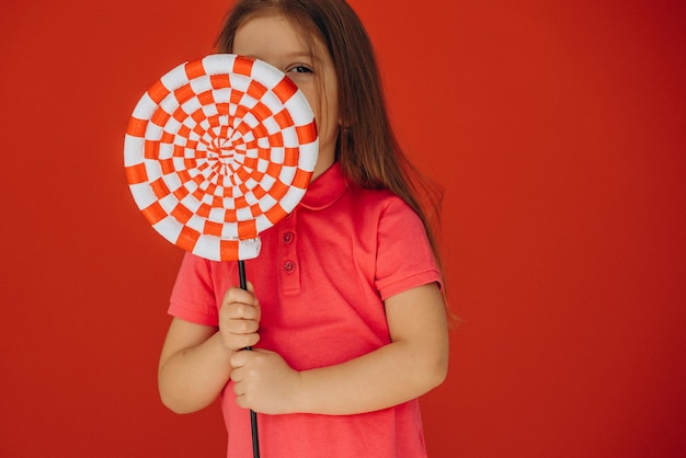 Bambina che tiene grande lecca-lecca isolato su sfondo rosso