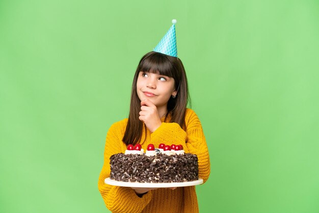 Bambina che tiene la torta di compleanno su sfondo chroma key isolato e alzando lo sguardo