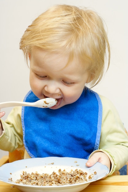 Bambina che tiene un cucchiaio tra le braccia e mangia un pap