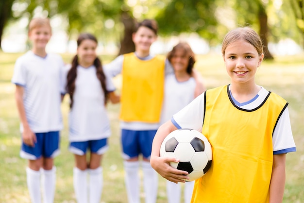 Bambina che tiene un pallone da calcio accanto ai suoi compagni di squadra