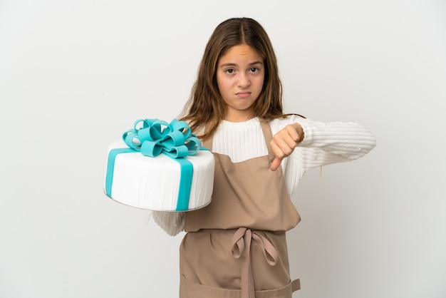 Bambina che tiene una grande torta su sfondo bianco isolato che mostra il pollice verso il basso con espressione negativa