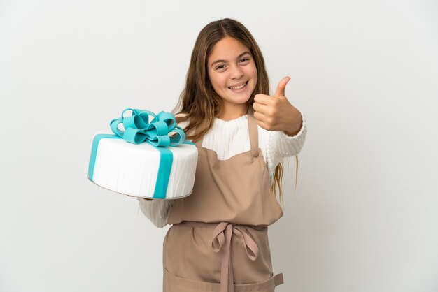 Bambina che tiene una grande torta su sfondo bianco isolato con il pollice in alto perché è successo qualcosa di buono