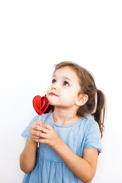 Bambina che tiene una lecca-lecca a forma di cuore, amanti, San Valentino, famiglia e cuore