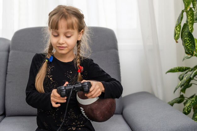 Bambina che tiene una palla da rugby e un joystick per giocare ai videogiochi