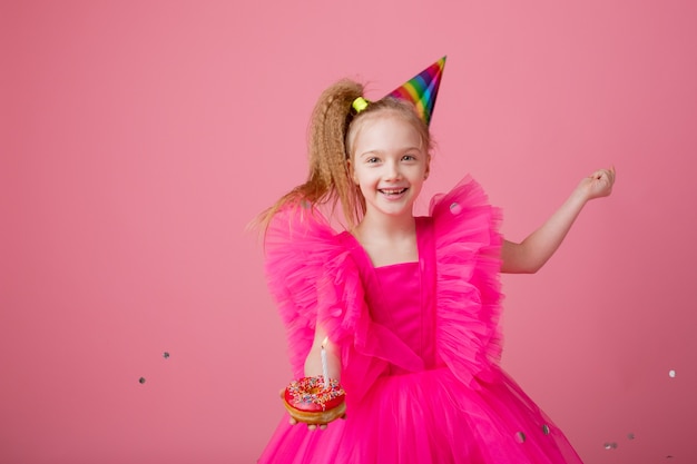 Bambina che tiene una torta festiva che soffia una candela su uno sfondo rosa che celebra il suo compleanno
