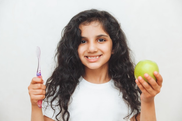 Bambina che tiene uno spazzolino da denti e una mela su sfondo bianco Il concetto di lavarsi i denti Il viso sorridente di una ragazza tiene una mela e uno spazzolino da denti Il viso felice del bambino si prende cura dell'igiene