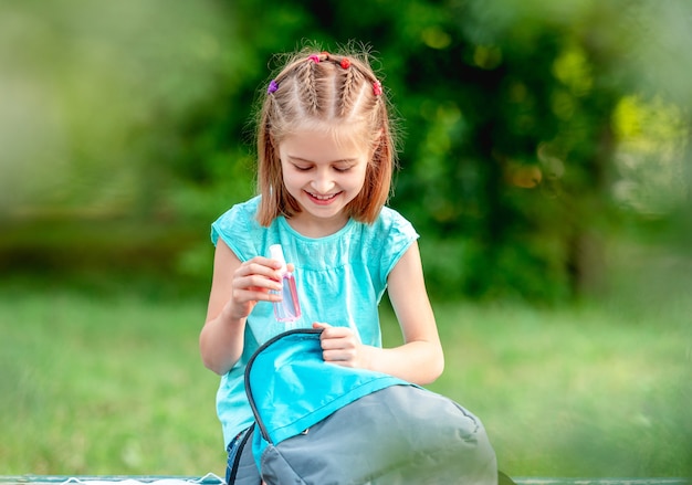 Bambina che toglie mascherina medica dallo zaino nel parco