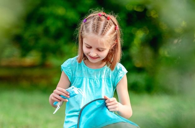 Bambina che toglie mascherina medica dallo zaino nel parco