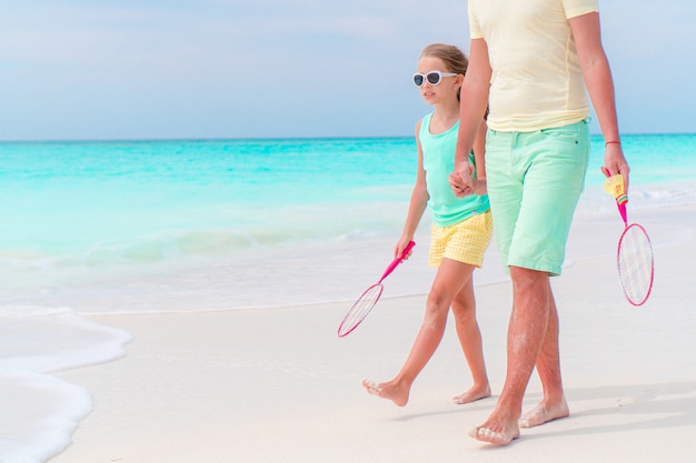 Bambina che va a giocare a tennis con il padre sulla spiaggia tropicale bianca