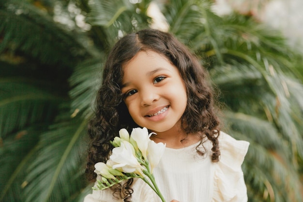 Bambina circondata da foglie tropicali Ritratto di un bambino swarthy con i capelli scuri Cosmetici naturali salute pulizia