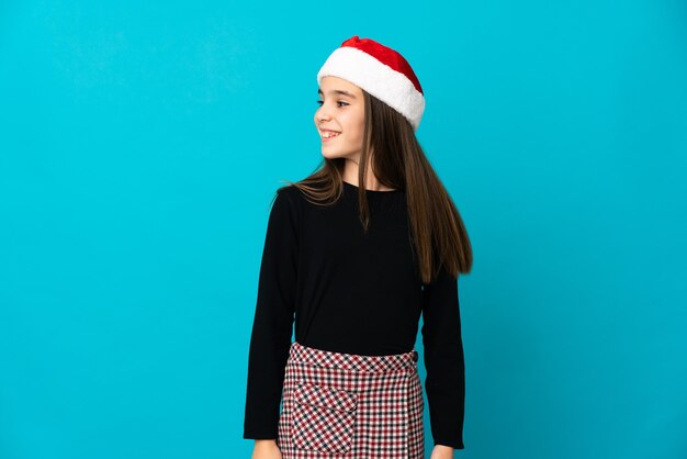 Bambina con cappello di Natale isolato guardando al lato e sorridente