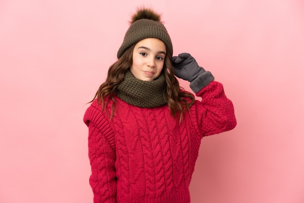 Bambina con cappello invernale isolato su sfondo rosa che ha dubbi