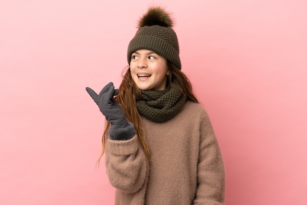 Bambina con cappello invernale isolato su sfondo rosa con l'intenzione di realizzare la soluzione sollevando un dito