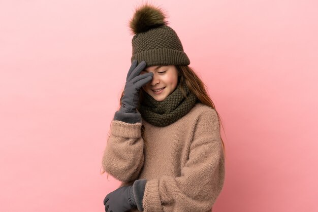 Bambina con cappello invernale isolato su sfondo rosa ridendo