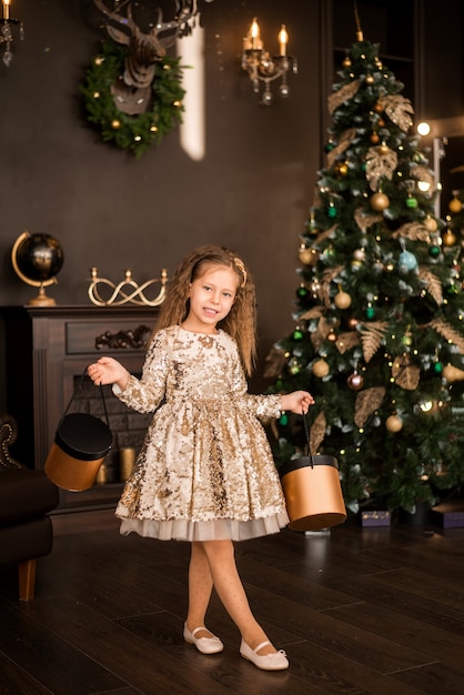Bambina con doni sullo sfondo di un albero di Natale. Un bambino in un elegante vestito d'oro