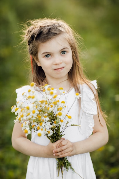Bambina con fiori Ragazza in giardino con un mazzo di camomilla