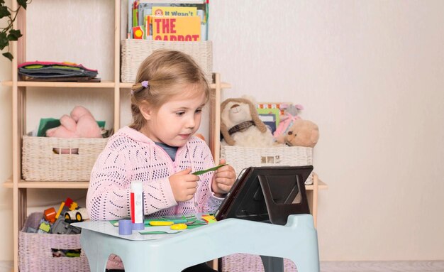 Bambina con forbici e colla Ritratto di una bambina carina che taglia una carta con tablet pc