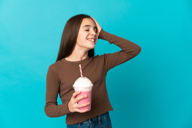 Bambina con frappè alla fragola isolato su sfondo blu sorridente molto