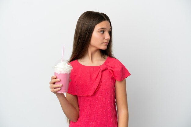 Bambina con frappè alla fragola sopra superficie bianca isolata che guarda al lato