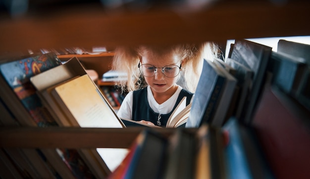 Bambina con gli occhiali alla ricerca di un libro in biblioteca