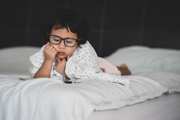 Bambina con gli occhiali sdraiata sul letto guardando tablet