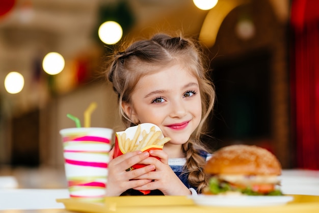 Bambina con hamburger, bibita gassata e patatine fritte