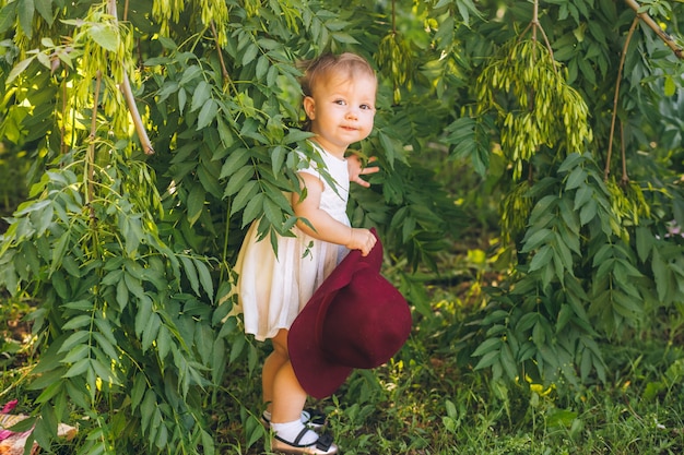 bambina con i capelli biondi in un abito bianco e cappello rosso della madre nel parco giornata di sole estivo