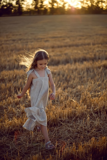 Bambina con i capelli lunghi che cammina attraverso il campo che indossa con i capelli lunghi durante il tramonto