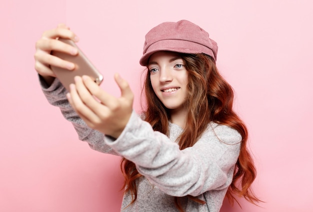 Bambina con i capelli ricci l che si fa un selfie isolato su sfondo rosa