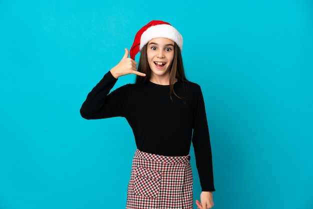 Bambina con il cappello di Natale isolato sulla parete blu che fa il gesto del telefono. Richiamami segno