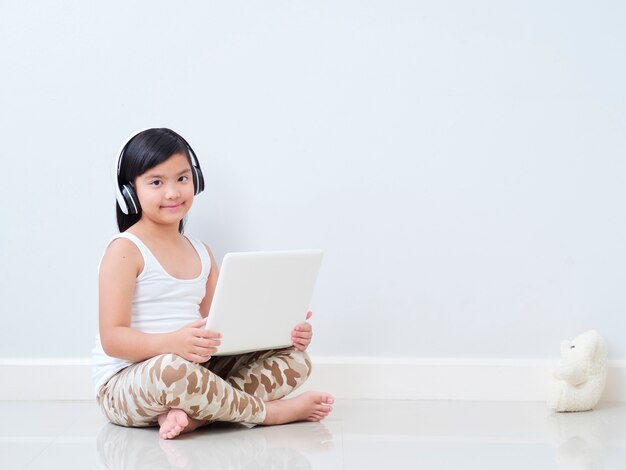 Bambina con il portatile seduto sul pavimento.