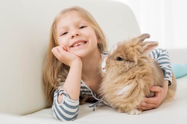 Bambina con il suo coniglietto sdraiato sul divano e abbracciarsi