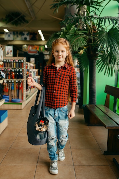 Bambina con il suo cucciolo in borsa, negozio di animali. Bambino che acquista attrezzature nel negozio di animali, accessori per animali domestici