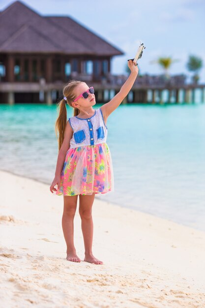 Bambina con l'aeroplano giocattolo nelle mani sulla spiaggia di sabbia bianca