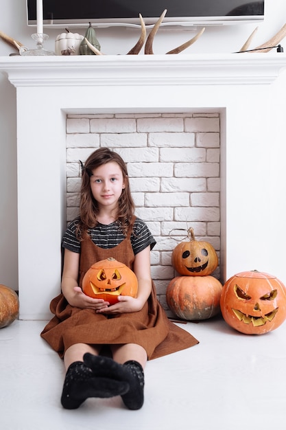 Bambina con la zucca intagliata su Halloween a casa seduto accanto al caminetto