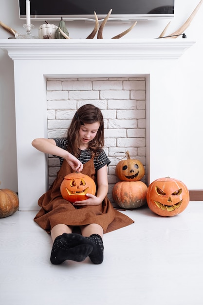 Bambina con la zucca intagliata su Halloween a casa seduto accanto al caminetto