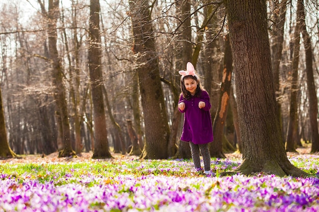 Bambina con le orecchie banny che fa capolino da dietro un albero nel parco