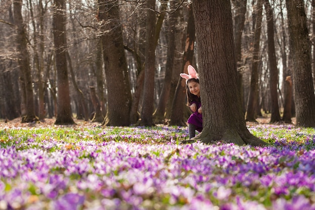 Bambina con le orecchie da banny che fa capolino da dietro un albero nel parco