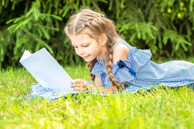 bambina con le trecce legge un libro sdraiato sull'erba verde del parco.