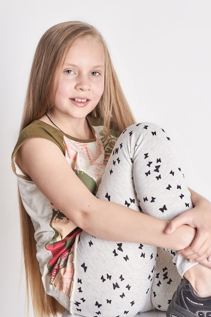 Bambina con lunghi capelli lussuosi, un bel sorriso. Emozioni di gioia sul viso. Ragazza in posa su sfondo chiaro. Look estivo