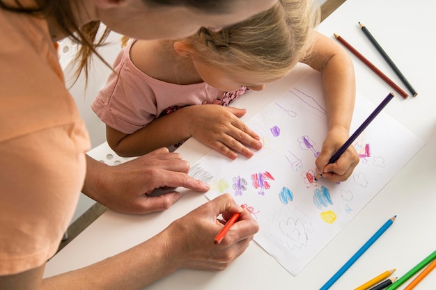 Bambina con mamma disegnare con matite colorate su carta bianca Vista dall'alto piatto laico