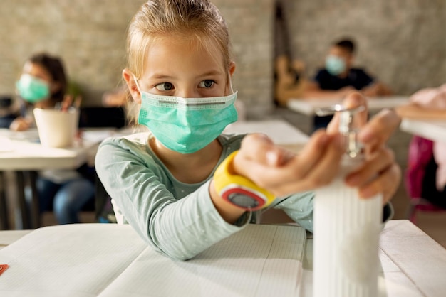 Bambina con maschera facciale che disinfetta le mani durante una lezione in classe