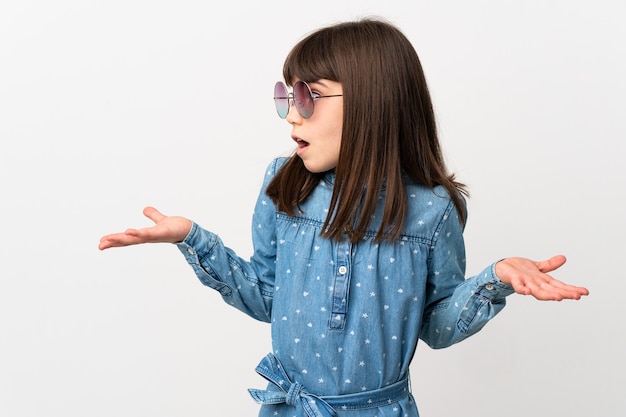 Bambina con occhiali da sole isolati su sfondo bianco con espressione di sorpresa mentre guarda di lato