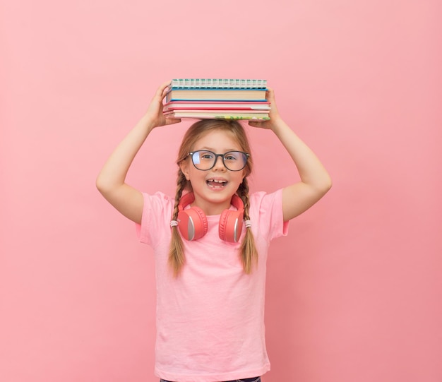 Bambina con occhiali e cuffie Pila di libri sulla testa su rosa Concetto di ritorno a scuola