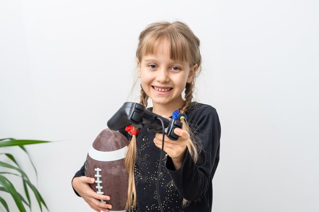 bambina con pallone da rugby e joystick per giocare ai videogiochi a casa