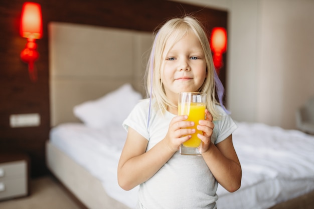 Bambina con un bicchiere di succo d'arancia fresco in camera da letto a casa. Un'infanzia davvero spensierata, tempo felice